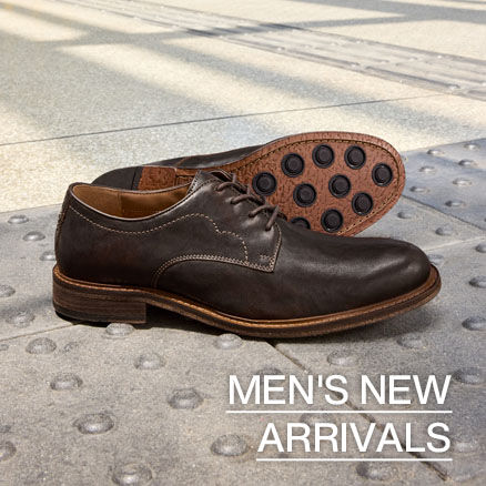 Pair of dark brown leather men's dress shoes displayed on a city sidewalk, with one shoe showing the textured rubber outsole. Text reads &ldquo;Men's New Arrivals.&rdquo;